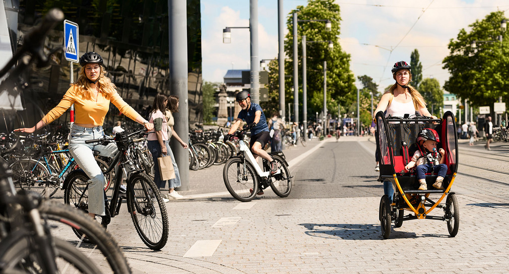 Mehrere Radfahrer fahren einen breiten Radweg an einer Straße entlang.