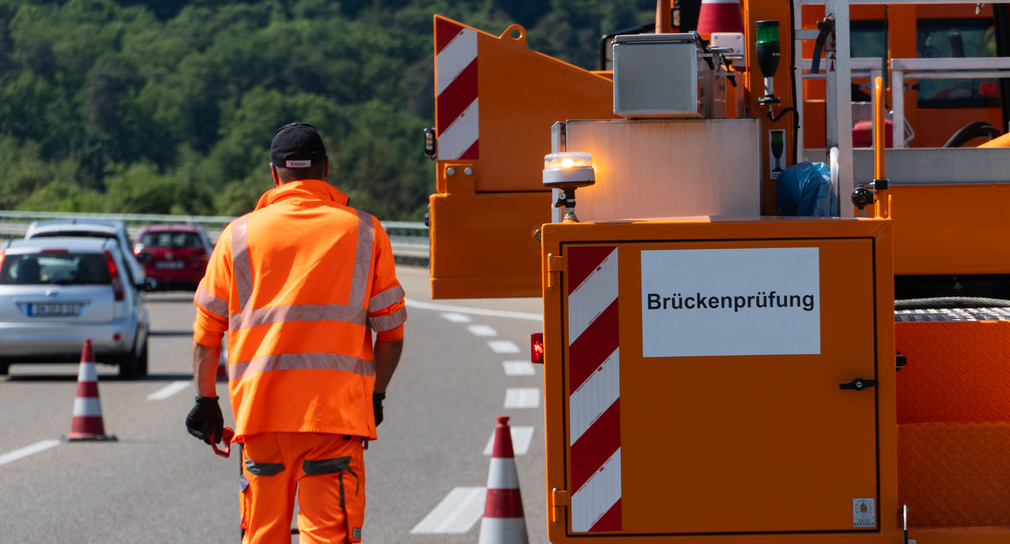 Ein Straßenwärter mit orangenen Klamotten läuft auf einer Brücke.