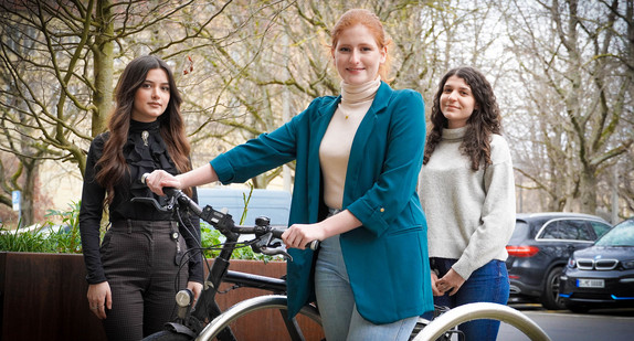 Drei Frauen stehen um ein Fahrrad nebeneinander.