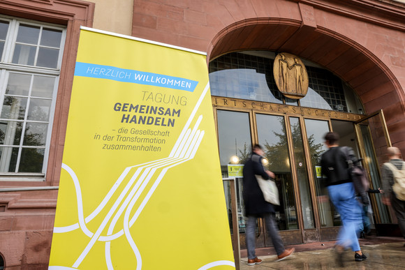 Zusammenhalt in der Transformation Tagung „Gemeinsam handeln“ Eingang zur Tagung in der Universität Mannheim mit einem Banner mit der Aufschrift „HERZLICH WILLKOMMEN - TAGUNG GEMEINSAM HANDELN – die Gesellschaft in der Transformation zusammenhalten“.