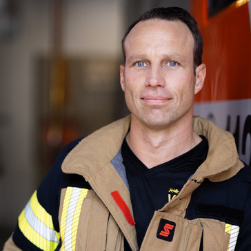 Portrait-Foto von Feuerwehrmann Kilian Wieczorek. Er lehnt in Einsatzkleidung an einem Feuerwehrauto.