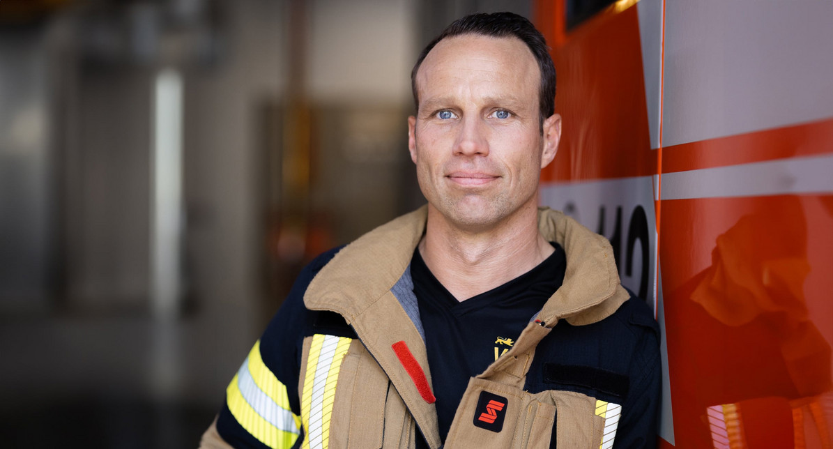 Portrait-Foto von Feuerwehrmann Kilian Wieczorek. Er lehnt in Einsatzkleidung an einem Feuerwehrauto.