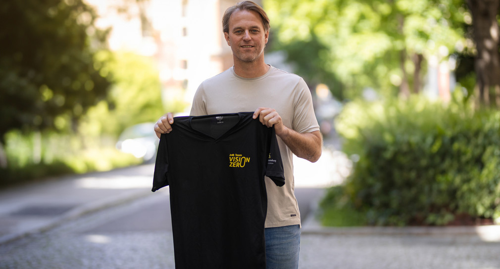 Timo Hildebrand hält ein schwarzes T-SHirt mit dem Logo von Team Vision Zero in die Kamera.