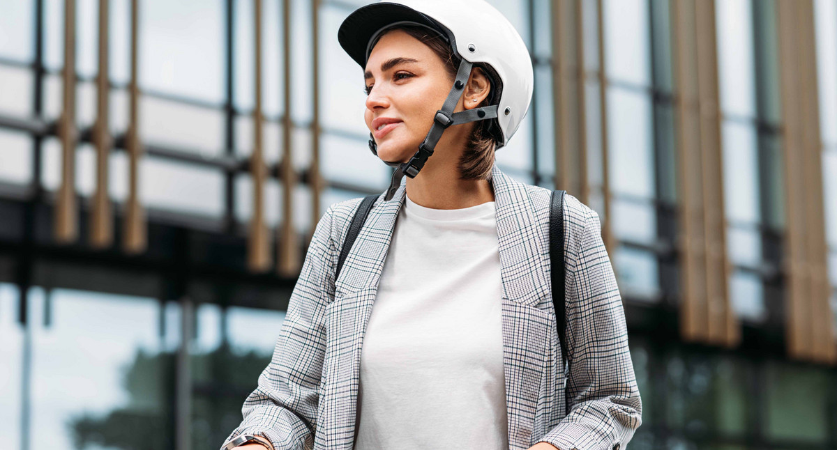 Frau im weißen Fahrradhelm hält einen Lenker eines Elektrorollers und schaut weg