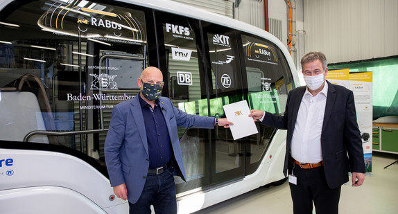 Verkehrsminister Winfried Hermann und Prof. Dr. Hans-Christian Reuss vom Forschungsinstitut für Kraftfahrwesen und Fahrzeugmotoren (FKFS) vor dem autonomen Shuttlebus