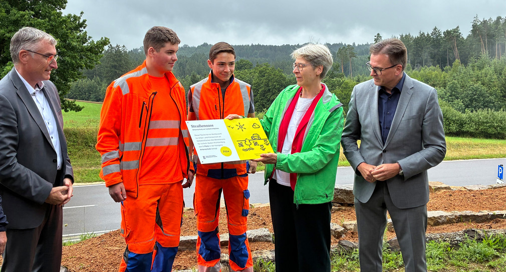 Staatssekretärin Elke Zimmer übergibt den Straßenwärter-Auszubildenden der Straßenmeisterei Ellwangen Maximilian Klos und Noah Wagner die Gewinnerplakette „Straßenoase“. Dabei sind Kreiskämmerer Karl Kurz und Landrat Joachim Bläse.