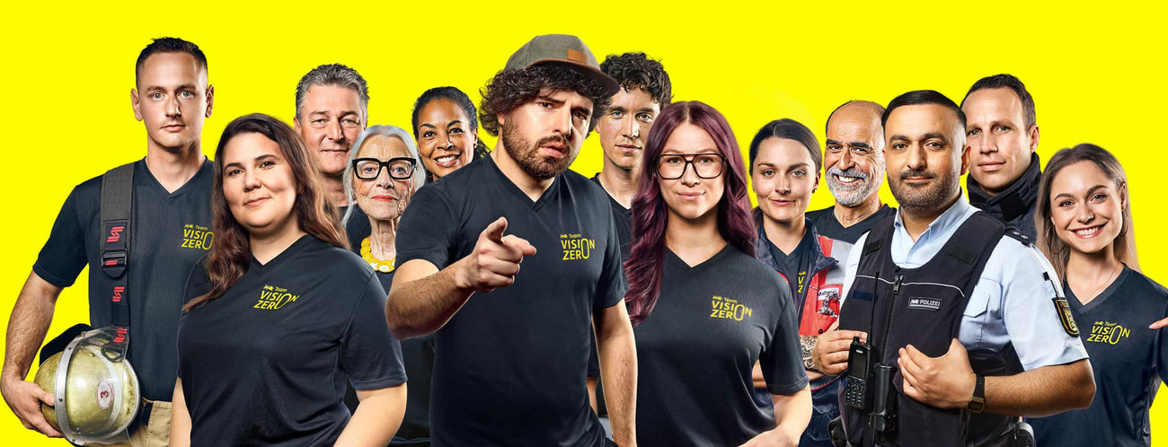 Ein Gruppenbild des Team Vison Zero. Zu sehen sind Feuerwehrleute, eine Rettungssanitäterin, ein Polizist, ein Fahrsicherheitstrainer, eine Fahrschullehrerin, Comedians, Moderator:innen und Bürger:innen verschiedenen Alters.