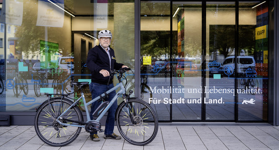 Verkehrsminister Winfried Hermann trägt einen Fahrradhelm und steht mit Fahrrad vor dem Eingang zum Verkehrsministerium.