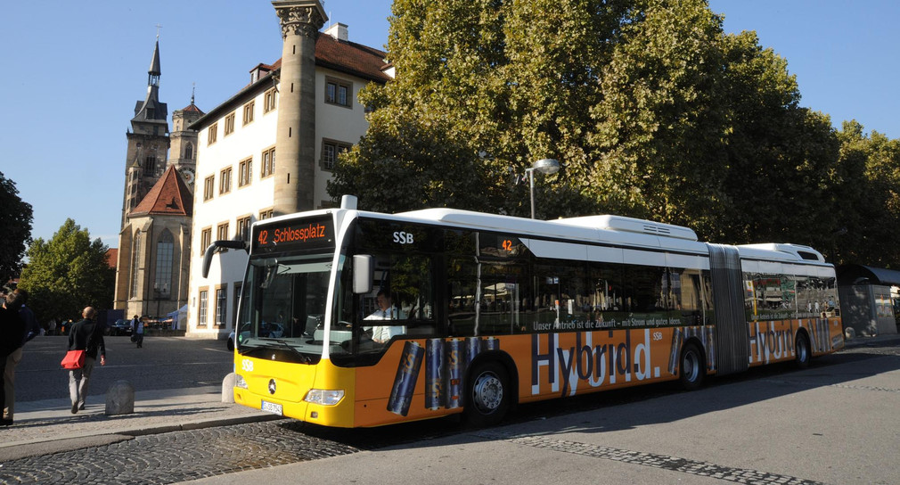 Gelber Bus der SSB mit der Aufschrift "Hybrid" hält an einer Haltestelle.