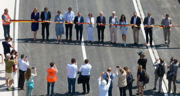Mehrere Menschen stehen in einer Reihe und schneiden ein Band durch. 