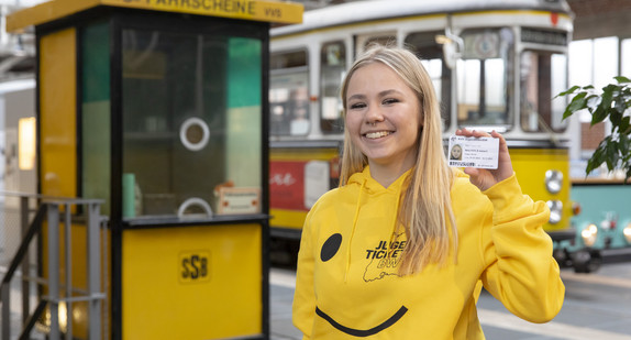 Junge Frau mit KVV-JugendticketBW, im Hintergrund alte Straßenbahnen.