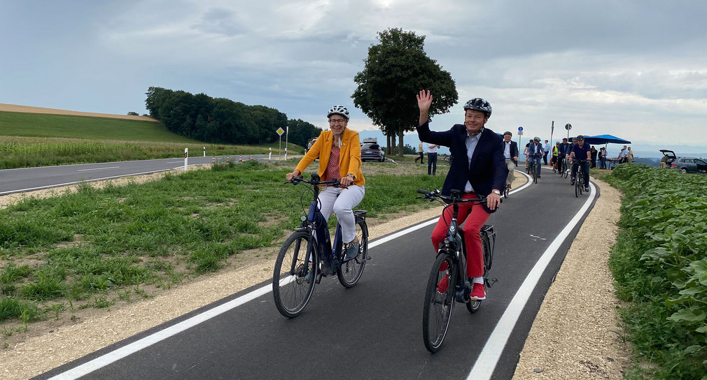 Staatssekretärin Elke Zimmer und Regierungspräsident Klaus Tappeser fahren mit Fahrrädern auf einem neuen Radweg. 