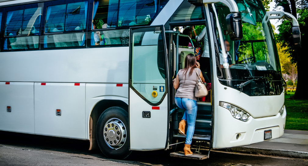 Frau mit Handy am Ohr steigt in weißen Reisebus ein