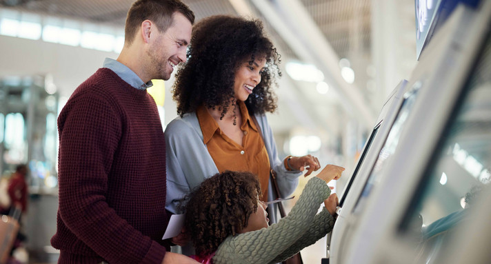 Selbstbedienung, Lächeln und Reisen mit gemischter Familie am Flughafen zum Einchecken, für Urlaub und weltweit. Technologie, digital und glücklich mit Eltern und Kind am Kiosk für Urlaubs-, Flug- und Ticketinformationen.