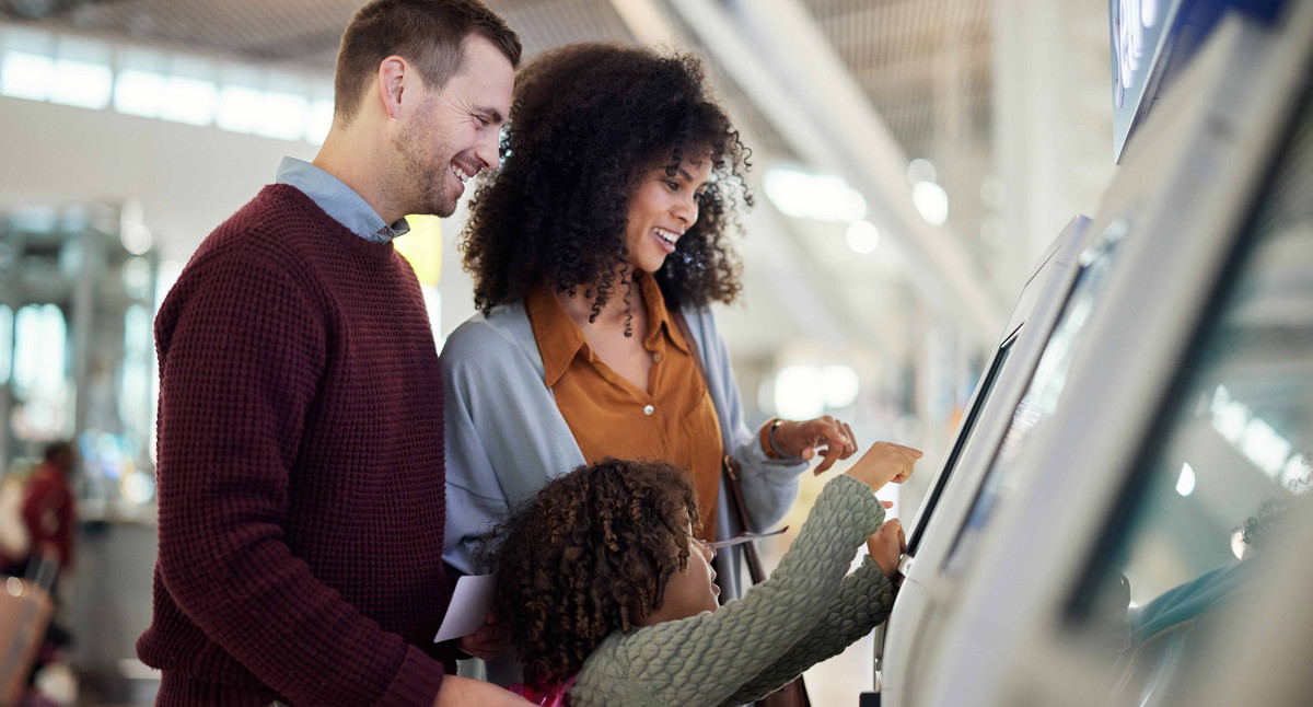 Selbstbedienung, Lächeln und Reisen mit gemischter Familie am Flughafen zum Einchecken, für Urlaub und weltweit. Technologie, digital und glücklich mit Eltern und Kind am Kiosk für Urlaubs-, Flug- und Ticketinformationen.