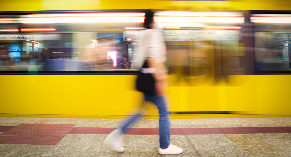 Verschwommenes Bild mit einer Frau, die an einem Bahnsteig entlangläuft während eine gelbe Bahn vorbeifährt.