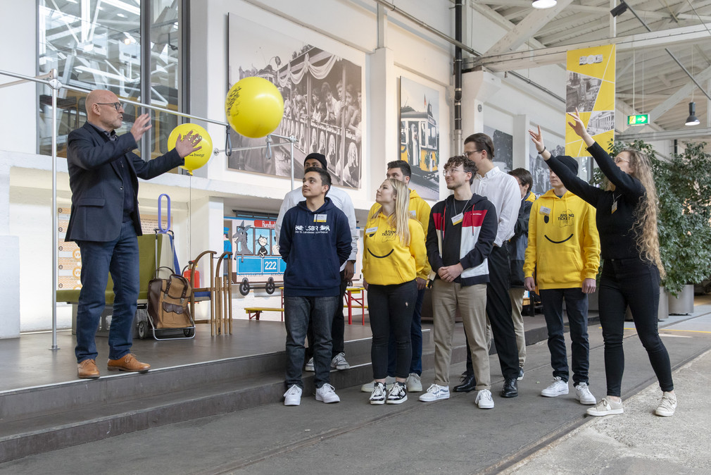 Minister Hermann und eine Gruppe junger Menschen werfen sich gelbe Luftballons mit JugendticketBW-Logo zu.