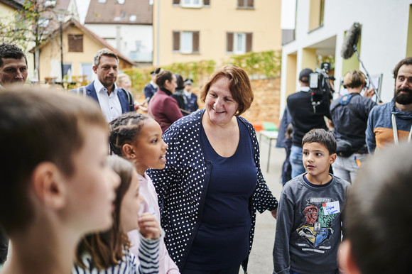 Verkehrssicherheit MOVERS – Aktiv zur Schule Ministerin Schopper mit mehreren Kindern im Gespräch. Weitere Menschen im HIntergrund.