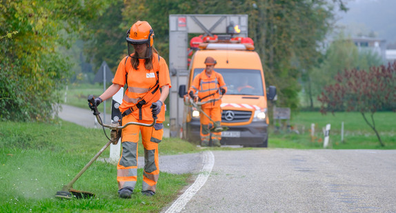 Eine Straßenwärterin mäht Gras am Straßenrand.