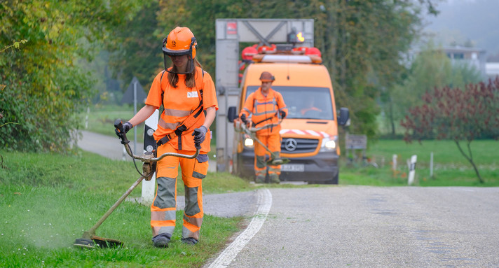 Eine Straßenwärterin mäht Gras am Straßenrand.
