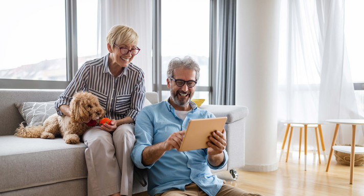 Glückliches, älteres Paar benutzt ein digitales Tablet, redet und lächelt zu Hause.