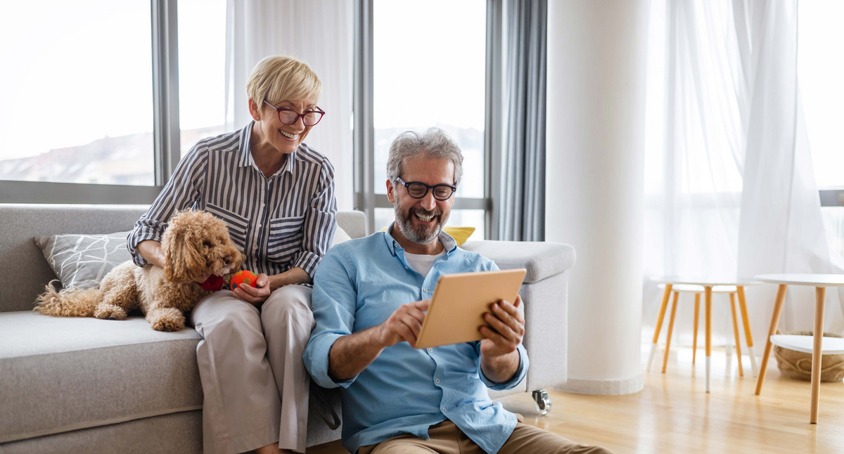 Glückliches, älteres Paar benutzt ein digitales Tablet, redet und lächelt zu Hause.