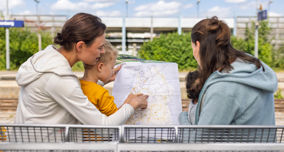Eine Familie mit kleinem Kind sitzt auf einer Bank an einem Bahnsteig und schaut auf eine Karte des Schienennetzes in Baden-Würrtemberg.
