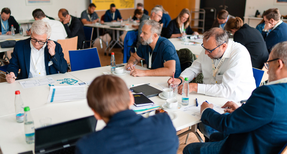 Eine Gruppe von M&auml;nnern und Frauen sitzen an einem Tisch und arbeiten.