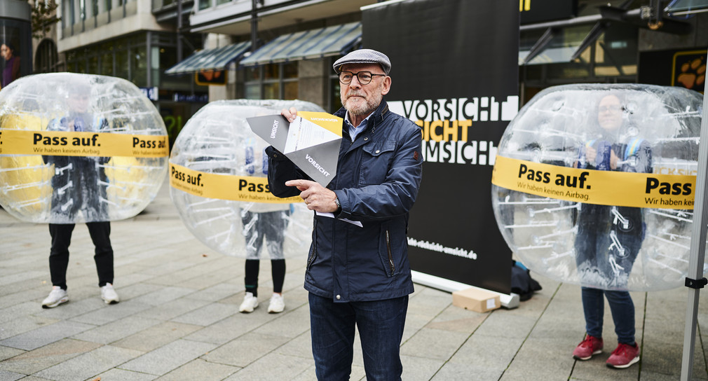 Minister Hermann präsentiert auf der Königsstraße den Flyer der Kampagne. Im Hintergrund stehen Menschen in sogenannten „Bumper Balls". 