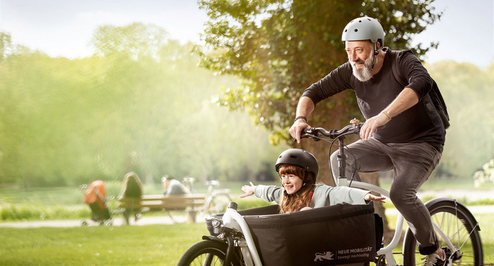 Mann fährt auf einem Lastenrad in dem ein Mädchen sitzt.