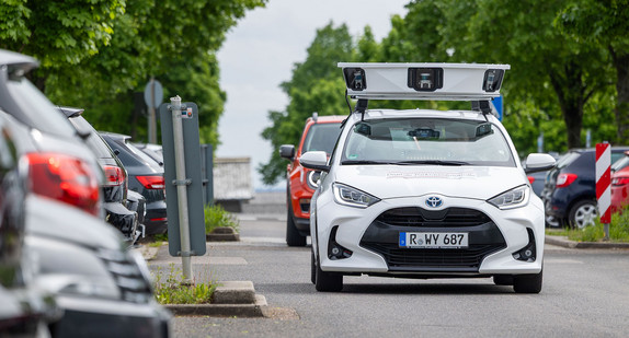 Ein Auto mit Kameras und Sensoren auf dem Dach fährt an Parkplätzen vorbei.