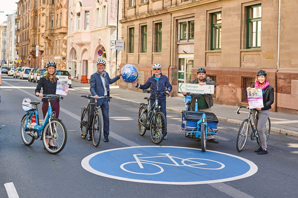 Verkehrsminister Hermann, Amtschef Frieß sowie Mitarbeiterinnen und Mitarbeiter des Landes für den Radverkehr stehen mit verschiedenen Fahrrädern auf einer Fahrradstraße. Hermann und Frieß halten gemeinsam eine Weltkugel.