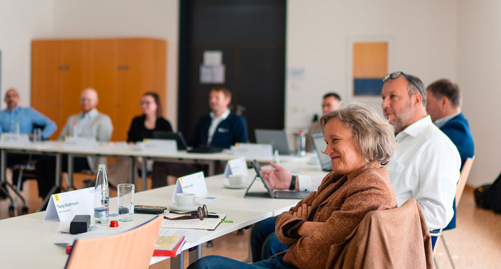 Eine Frau sitzt an einem Tisch und hört einem Vortrag zu.