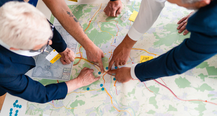 Mehrere Menschen beugen sich über eine Karte und zeigen mit dem Finger auf einen Ort.