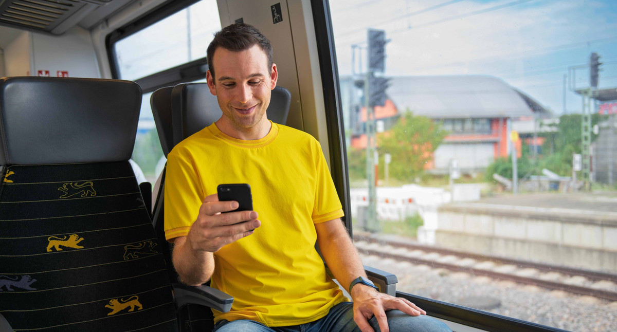 Ein Mann sitzt in einem Zug und sieht auf sein Smartphone.