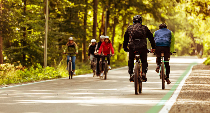 Mehrere Radfahrer:innen fahren auf einem breiten Fahrradweg aneinander vorbei.