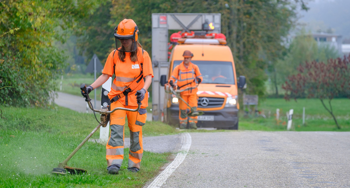 Eine Straßenwärterin mäht Gras am Straßenrand.