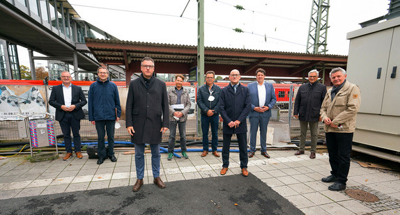 Mehrere Menschen stehen vor einem Zaun am Bahnhof Ulm. Dahinter liegt das Gleisfeld mit den Bahnsteigen.