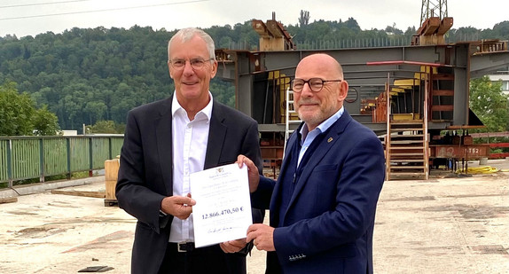 Dr. Jürgen Zieger, Oberbürgermeister der Stadt Esslingen am Neckar, und Landesverkehrsminister Winfried Hermann präsentieren vor einer Brückenbaustelle den Förderbescheid des Landes über knapp 13 Millionen Euro für den Ersatzneubau der Hanns-Martin-Schleyer-Brücke. 