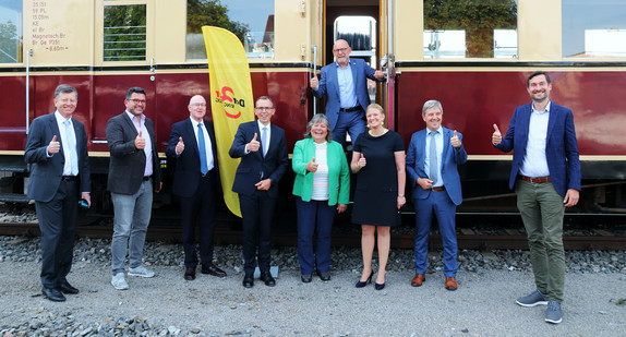 Mehere Menschen stehen vor einem Zug zu einem Gruppenbild zusammen.