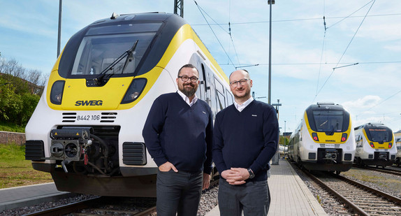 Zwei Lokführer stehen am Kopf eines Zuges der SWEG und lachen in die Kamera.