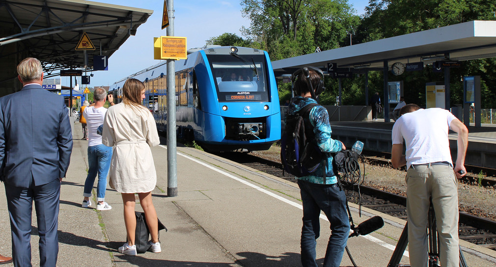 Ein blauer Zug fährt an einem Bahnsteig ein.