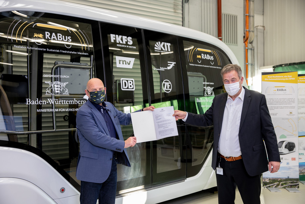 Verkehrsminister Winfried Hermann und Prof. Dr. Hans-Christian Reuss (FKFS) mit Förderschreiben vor dem autonomen Shuttlebus 
