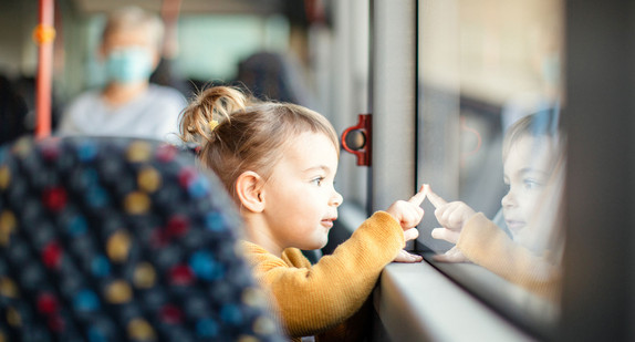 Ein kleines Mädchen sitzt in einem Bus und schaut zum Fenster hinaus.