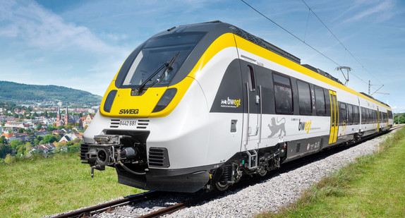 Elektrischer Zug in schwarz-gelbem Design fährt durch eine grüne Landschaft.