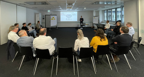 Eine Gruppe sitzt im Stuhlkreis zusammen und verfolgt eine Präsentation.