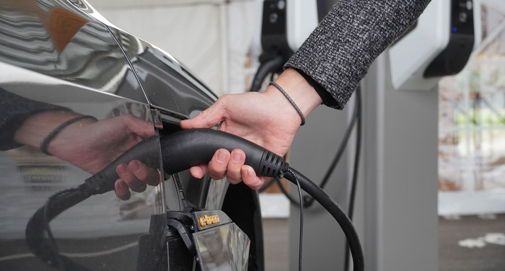 Eine Hand steckt ein Stromkabel in ein E-Auto.