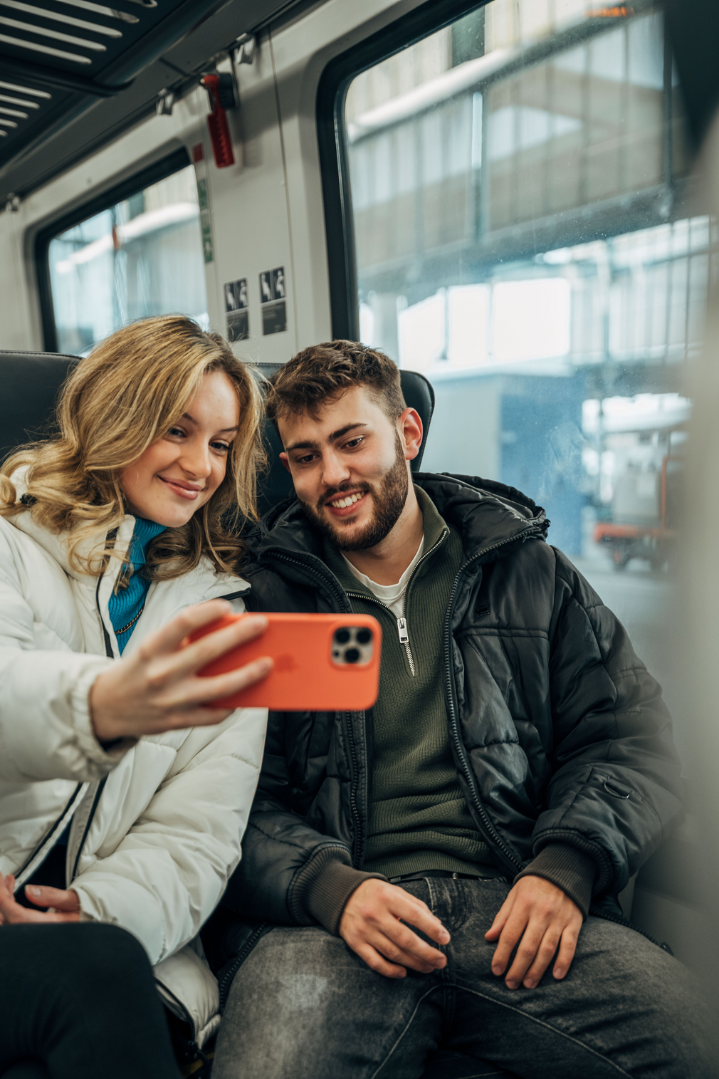 Eine junge Frau und ein junger Mann in einem Zug, die gerade ein Selfie schießen.