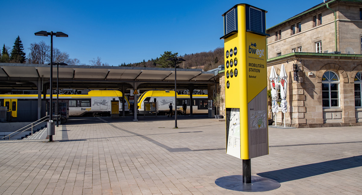 Bahnhofsvorplatz auf dem eine große gelbe Informationssäule mit Informationen zu den regionalen Mobilitätsangeboten.