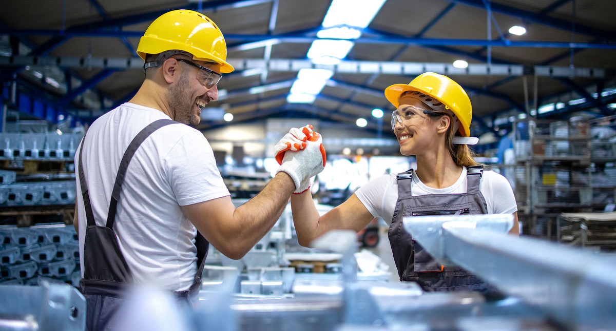 Ein Mann und eine Frau die in einer Werkshalle arbeiten, schlagen erfreut ihre Hand zusammen.